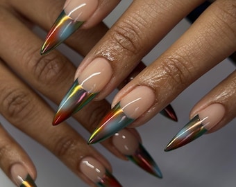 Puede incluir: Uñas en forma de estilete con una base de color nude y una punta con degradado metálico e iridiscente que cambia entre tonos rojos, dorados y azules. El diseño crea una apariencia afilada y puntiaguda con un acabado brillante.