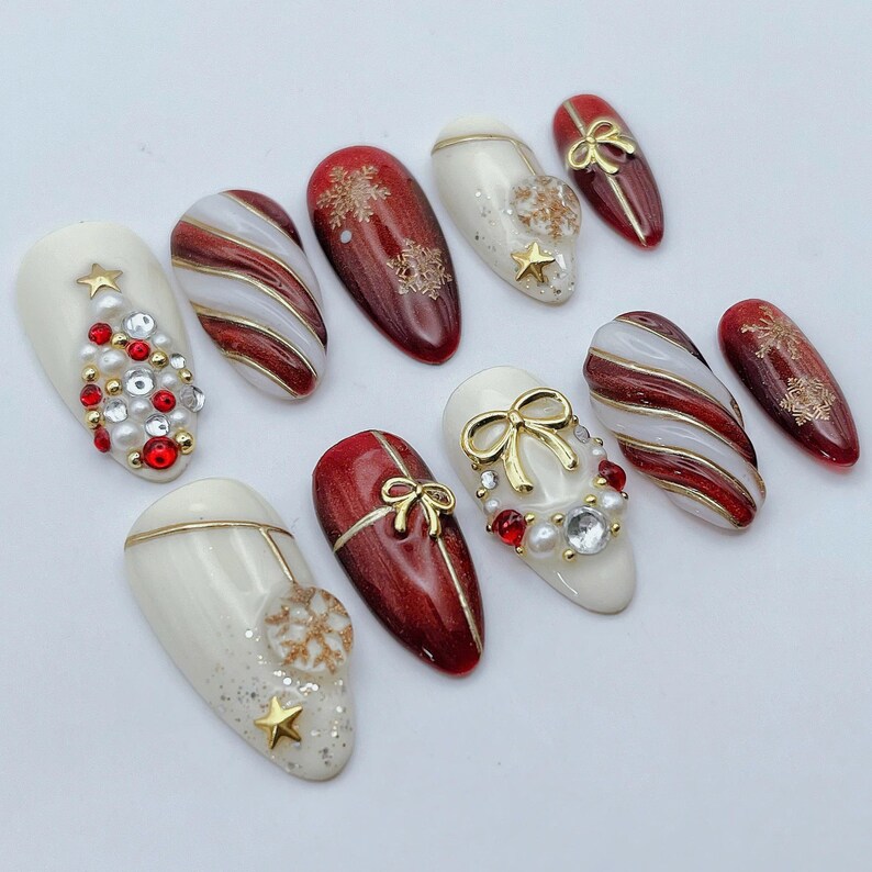 May include: A set of ten almond-shaped press-on nails featuring a holiday theme. The designs include red and white candy cane stripes, gold snowflakes, pearl and rhinestone accents, gold bows, and a Christmas tree motif made of small gems.