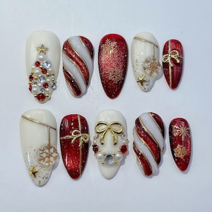 May include: A set of ten press-on nails featuring Christmas themes in red, white, and gold. Designs include candy cane stripes, glittery red surfaces with gold snowflakes, cream bases with pearl and rhinestone accents, and gold bow embellishments.