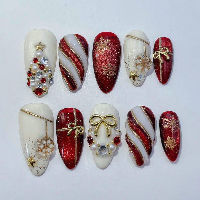 May include: A set of ten press-on nails featuring Christmas themes in red, white, and gold. Designs include candy cane stripes, glittery red surfaces with gold snowflakes, cream bases with pearl and rhinestone accents, and gold bow embellishments.