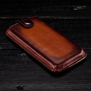 May include: A brown leather phone case with a red stitching detail and a silver button closure.
