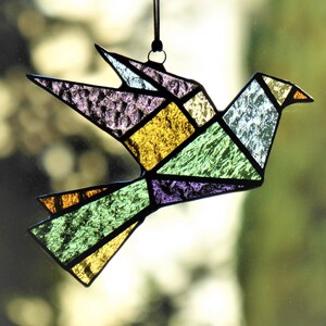 Pode incluir: Apanhador de sol de p&aacute;ssaro em vitral com design geom&eacute;trico de origami. O p&aacute;ssaro apresenta uma variedade de cores, incluindo amarelo, verde, roxo e azul. Ele pendura de um cord&atilde;o preto, perfeito para decora&ccedil;&atilde;o de janelas ou paredes.