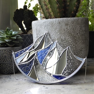 Pu&ograve; includere: Un acchiappasole in vetro colorato a forma di semicerchio con un design a catena montuosa. L'oggetto &egrave; composto da pannelli di vetro blu testurizzato, vetro a specchio trasparente e vetro iridescente, uniti da linee di saldatura argentate.