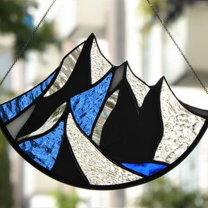 Pu&ograve; includere: Un acchiappasole in vetro colorato a forma di semicerchio con un design a catena montuosa. L'oggetto &egrave; composto da segmenti di vetro trasparente testurizzato, vetro nero solido e vetro blu vibrante uniti da linee di saldatura in metallo scuro.