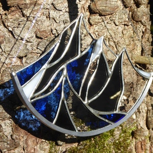 Pu&ograve; includere: Un acchiappasole in vetro colorato con un design a catena montuosa dai picchi frastagliati. L'oggetto &egrave; composto da segmenti di vetro blu traslucido, nero opaco e bianco uniti da linee di saldatura in metallo argentato e include una catenella.