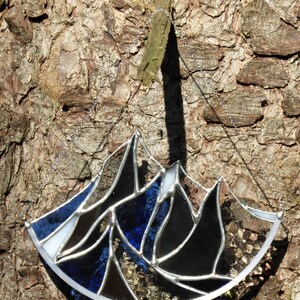 Pu&ograve; includere: Un acchiappasole in vetro colorato a forma di semicerchio con un design a catena montuosa. L'oggetto &egrave; composto da segmenti di vetro nero, blu scuro e bianco uniti da linee di saldatura in metallo argentato e include una sottile catena.