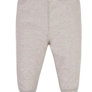 May include: Light grey baby trousers with an elasticated waistband and ribbed cuffs at the ankles. The trousers are made of a soft, knitted fabric and have a vertical seam down the centre of each leg.