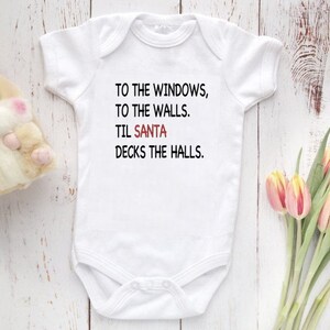May include: White baby onesie with black text that reads "To the windows, to the walls. Til Santa decks the halls."