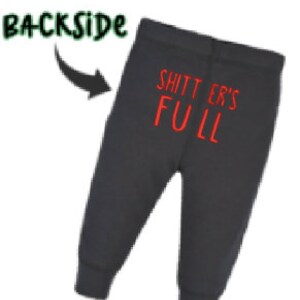 May include: Black sweatpants with the text "SHITTER'S FULL" in red on the back. The word "BACKSIDE" is written in green above the sweatpants with an arrow pointing to the text. The sweatpants have a fitted ankle.