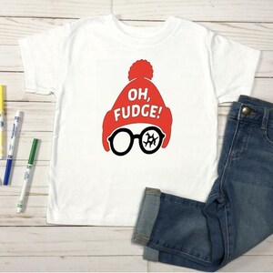 May include: White t-shirt with a red hat and glasses graphic. The graphic includes the text "OH, FUGE!". The shirt is paired with blue denim jeans. Colorful markers are scattered around the shirt.