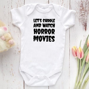 May include: White baby onesie with black text that reads "Let's cuddle and watch horror movies".