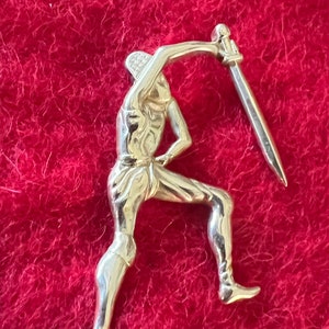 Pode incluir: Figurinha de metal prateado de uma pessoa segurando uma espada, em pé sobre uma superfície vermelha e felpuda.
