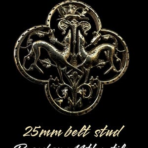 Pode incluir: Um botão de cinto de metal dourado de 25 mm com um design detalhado de dois cães estilizados perseguindo um veado, tudo dentro de uma moldura de trevo de quatro folhas. O texto "Based on a 14th c. tile" está abaixo do botão.