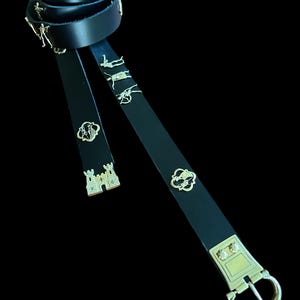 May include: A black leather belt with a gold buckle and decorative metal accents. The belt is coiled and laid out flat, showing the details of the buckle and accents.