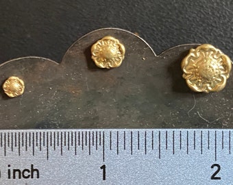 Op de afbeelding: Drie goudkleurige metalen decoratieve accenten in de vorm van een bloem, in verschillende maten, getoond op een grijs oppervlak met een liniaal voor schaal.