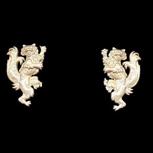 May include: Two gold-colored, ornate squirrel-like figurines, each standing upright with a detailed design. The background is solid black, highlighting the intricate details of the figurines. The figures appear to be made of metal.