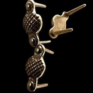 May include: Two gold-toned metal decorative pieces with a textured, circular design. The pieces have two prongs on the back for attaching to a surface.