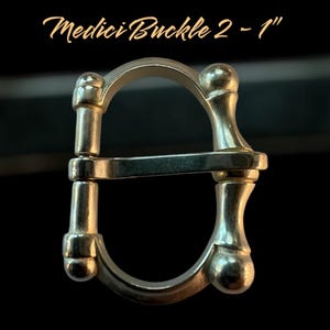 Puede incluir: Una hebilla de metal plateada con un diseño en forma de D. La hebilla tiene 2,5 cm de ancho y un acabado liso y pulido. Medici Buckle 2 - 1"