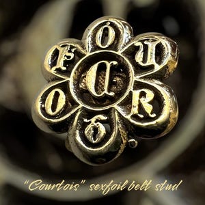 May include: A gold-colored metal belt stud in the shape of a flower with the letters "FOUR" surrounding a central "C".