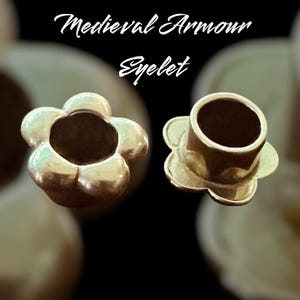 May include: Two gold-colored metal eyelets in the shape of a flower. The eyelets are used for attaching fabric or leather to other materials.