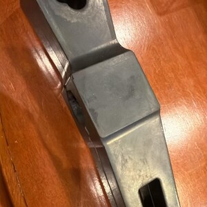 Puede incluir: Un objeto geom&eacute;trico gris oscuro con un agujero en forma de flor en la parte superior y una abertura rectangular en el lateral. El objeto tiene un acabado liso y mate y parece estar hecho de un material s&oacute;lido.