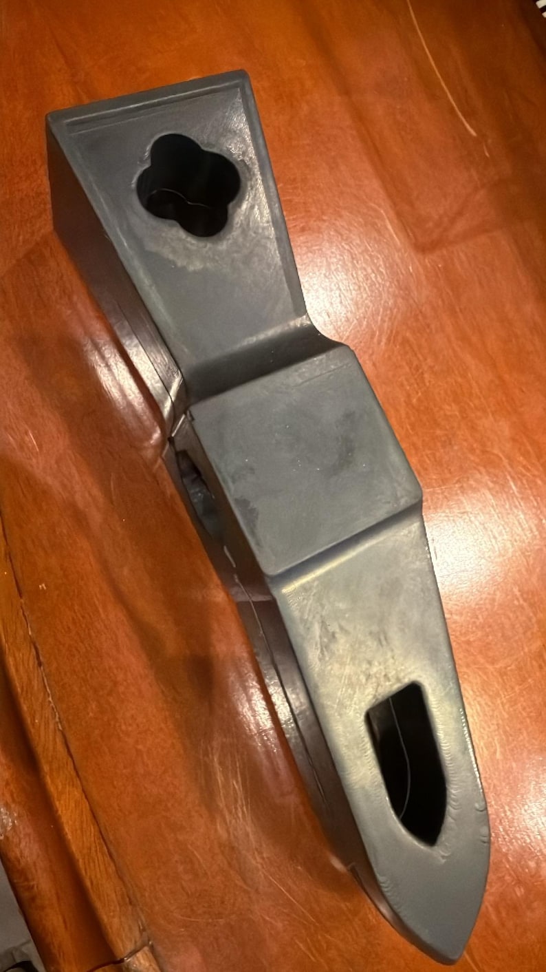 Puede incluir: Un objeto geom&eacute;trico gris oscuro con un agujero en forma de flor en la parte superior y una abertura rectangular en el lateral. El objeto tiene un acabado liso y mate y parece estar hecho de un material s&oacute;lido.