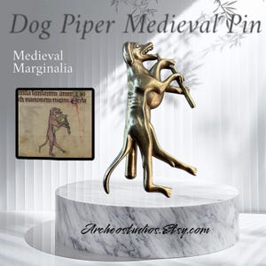May include: A gold-toned metal pin depicting a dog playing a pipe. The dog is standing on its hind legs and holding the pipe in its mouth. The pin is a replica of a medieval marginal illustration. The text "caula faanloum ameno di onarionem meam Ecda" is visible in the background.