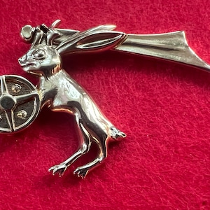 May include: A silver-toned rabbit figurine with wings and a shield. The rabbit is holding a round shield with a star design.