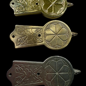 May include: Three decorative metal clasps with floral and geometric designs. The clasps are in gold and silver tones, each featuring a circular element with a flower-like pattern. The rectangular ends have intricate leaf patterns.