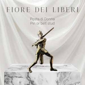 May include: A gold-toned metal pin or belt stud featuring a stylized figure of a crowned warrior holding a sword. The figure is standing in a fighting pose with one leg forward and the other leg back. The pin is labeled "Fiore Dei Liberi" and "Posta di Donna".