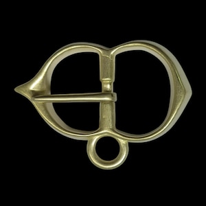 May include: A gold-toned metal buckle with a heart-shaped frame and a D-ring. The buckle has a pointed tip on each side.