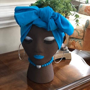 May include: A brown ceramic planter shaped like a woman's head with a blue turban and a blue beaded necklace. The planter is filled with green succulents.