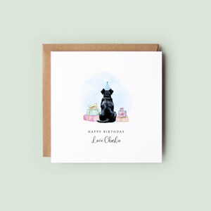 Pu&ograve; includere: Biglietto di auguri quadrato con un'illustrazione ad acquerello di un cane nero con un cappello da festa, seduto davanti a dei regali confezionati. Il biglietto recita "Happy Birthday, Love Charlie" in elegante calligrafia. Sfondo in cartoncino marrone.