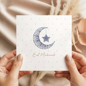 Elegant square Eid Mubarak card with a navy patterned crescent moon and hanging star, dotted gold stars on a white background and Eid Mubarak text in gold script.