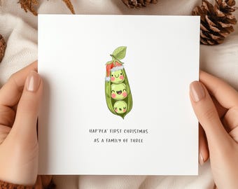 Könnte beinhalten: Eine weiße Weihnachtskarte mit dem Text "Hap'pea' First Christmas As A Family of Three." Die Karte zeigt eine Cartoon-Illustration von drei Erbsen in einer Schote, jede mit einem lächelnden Gesicht. Die oberste Erbse trägt einen Weihnachtsmütze.