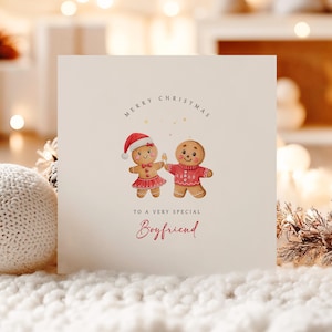 May include: A cream Christmas card with the text "MERRY CHRISTMAS" and "TO A VERY SPECIAL Boyfriend". The card features illustrations of gingerbread people wearing festive outfits. The card is on a white surface.