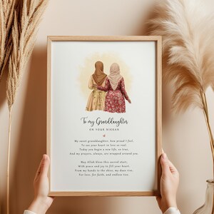 May include: A framed print featuring a watercolour illustration of two women in traditional dress, embracing. The text reads "To my Granddaughter on your Nikkah" with a poem below. The frame is light brown.