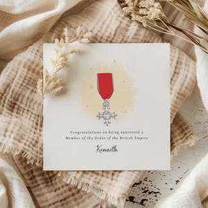 Peut inclure: Carte de vœux avec une illustration à l'aquarelle de la médaille de l'Ordre de l'Empire britannique. La carte contient le texte "Félicitations pour votre nomination en tant que Membre de l'Ordre de l'Empire britannique" et le nom "Kenneth".