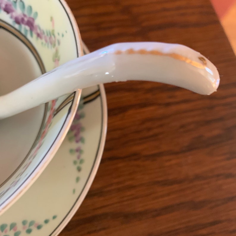 May include: A white porcelain soup spoon with a gold trim on the handle. The spoon is resting on a set of two white porcelain bowls with floral designs.