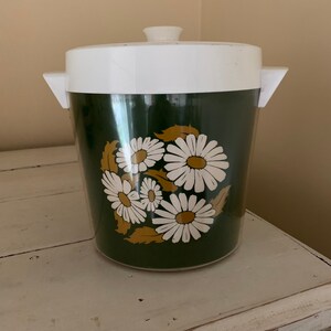 Op de afbeelding: Een groene en witte plastic ijs emmer met een madeliefjespatroon. De emmer heeft een wit deksel met een knop aan de bovenkant.