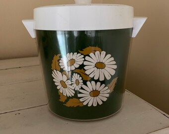 May include: A green and white plastic ice bucket with a daisy pattern. The bucket has a white lid with a knob on top.