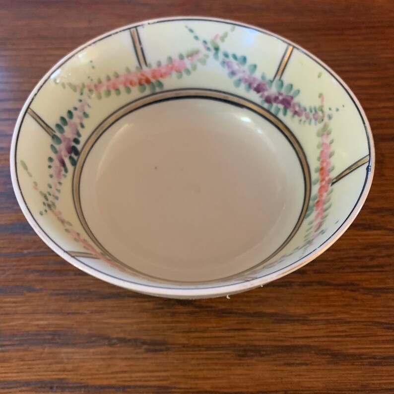 May include: A small, white ceramic bowl with a floral design. The bowl has a gold rim and a blue and green floral pattern.