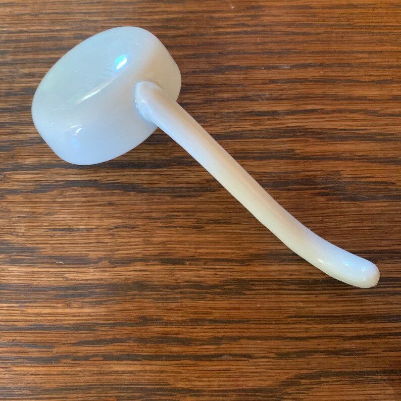 May include: White ceramic ladle with a long, curved handle. The ladle is on a wooden surface.