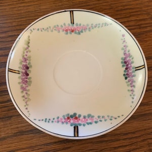 May include: White porcelain saucer with a gold trim and a floral design in shades of pink, purple, and green.
