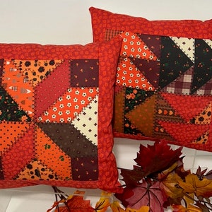 May include: Two red and orange patchwork throw pillows with a geometric pattern. The pillows are made of different fabrics with various patterns, including floral, plaid, and polka dots.