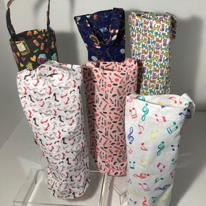 May include: Six different wine bottle totes with various patterns. The totes are made of fabric and have a drawstring closure. The patterns include musical notes, lips, high heels, cats, and nautical designs.