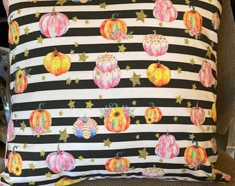 May include: A white and black striped pillow with a gold glitter pattern and watercolor pumpkins in various colors. The pumpkins have floral details and are scattered across the pillow.