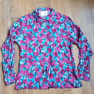 May include: A long-sleeved button-down shirt with a vibrant floral pattern. The shirt features a repeating design of pink flowers and turquoise leaves on a white background. The collar and cuffs are visible.