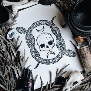 May include: Black and white illustration of a skull surrounded by two snakes, with crescent moon shapes above and below the skull. The illustration is on a white background.