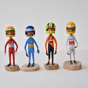 Op de afbeelding: Vier handgeschilderde beeldjes van raceautocoureurs met helmen en racepakken. De beeldjes staan op houten voetstukken.